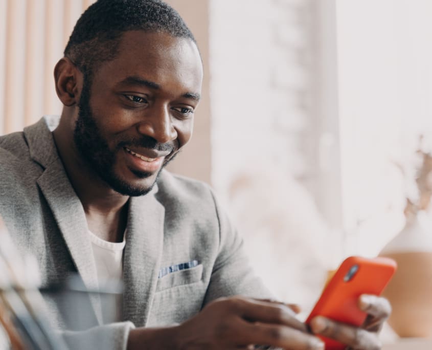 Smiling african american businessman using mobile, chatting online while sitting at office desk